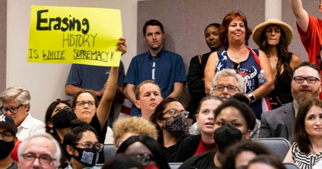 Person holds sign that says "Erasing history is white supremacy"